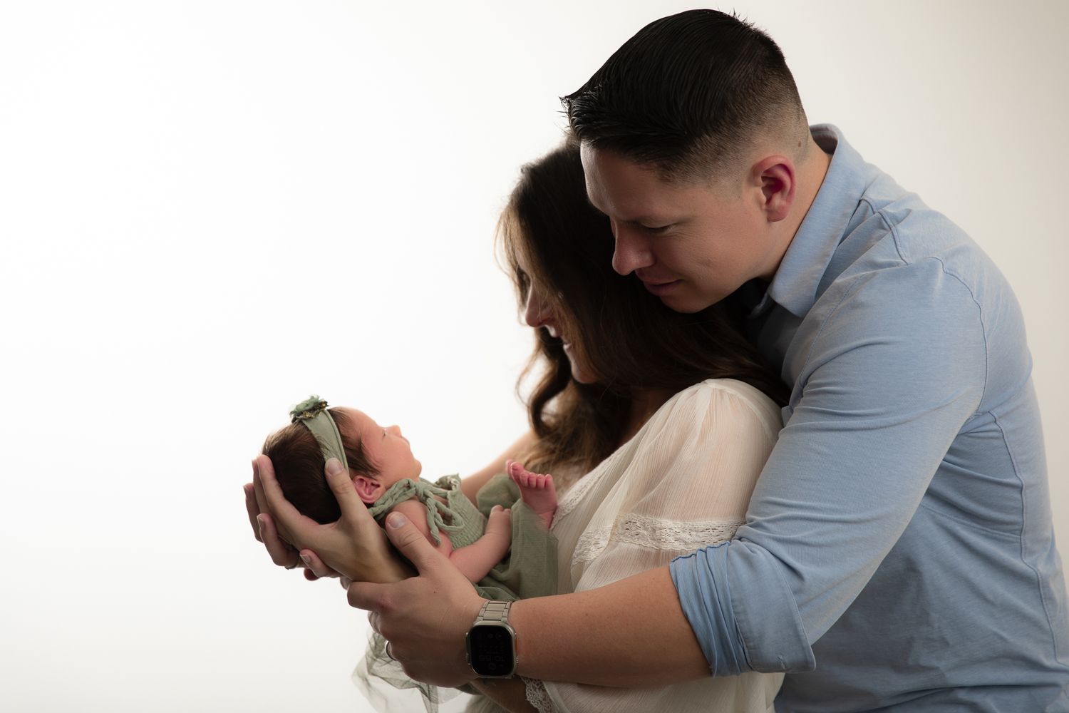 A couple tenderly holds their newborn baby together against a white studio background.