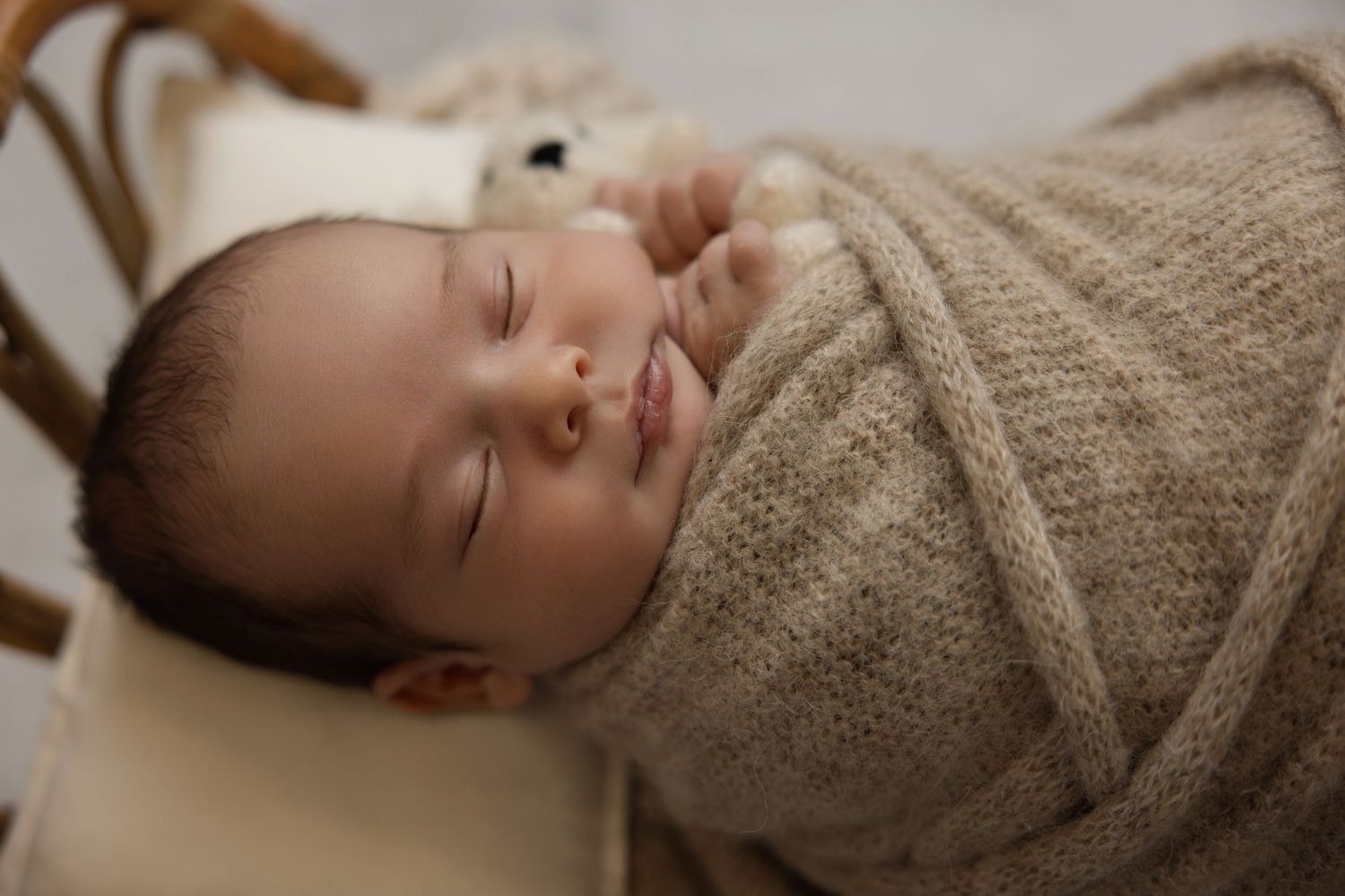 Peaceful newborn baby swaddled in a soft beige knit wrap, sleeping soundly with a gentle smile.