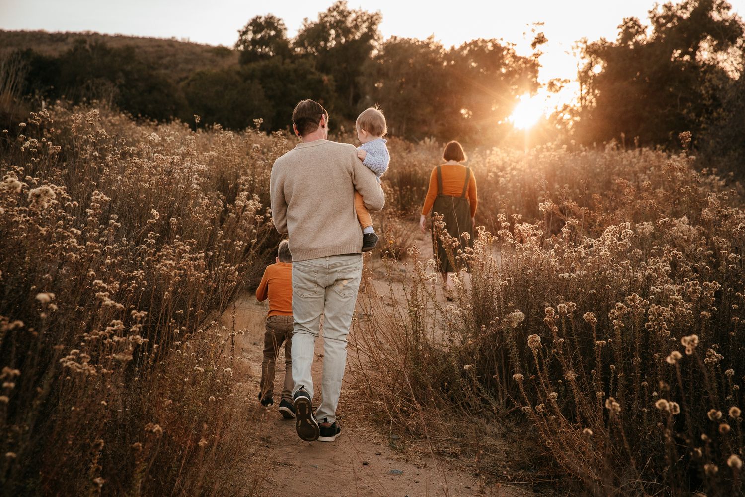 Family walking along a sunlit wildflower trail at golden hour with young children in warm tones in Bonsall CA