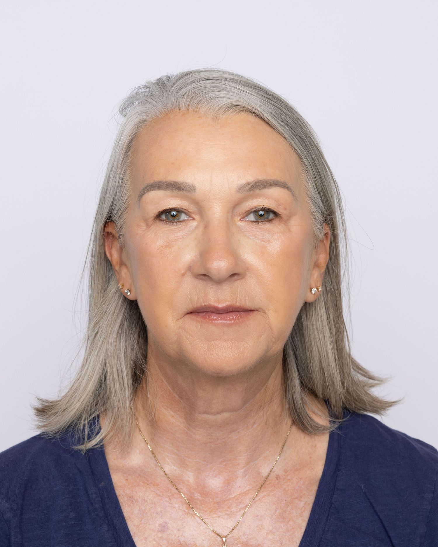 Older woman with gray hair wearing a navy top and gold necklace poses for a professional headshot photo.