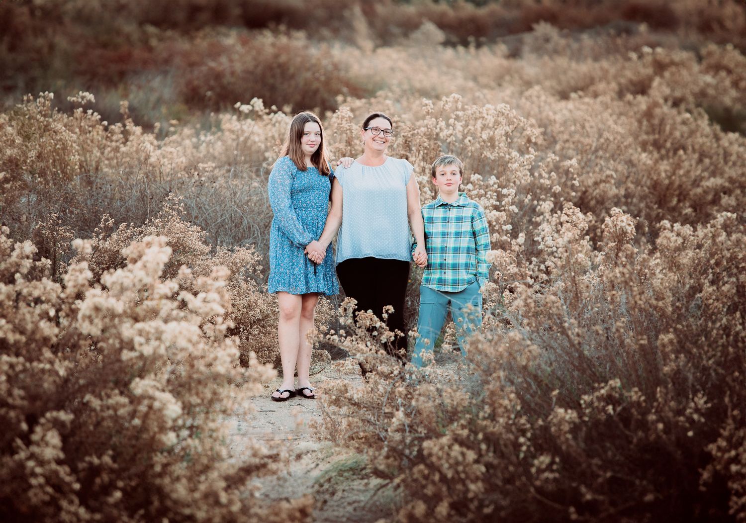 Family of three poses together in a golden field of wildflowers during outdoor photo session.