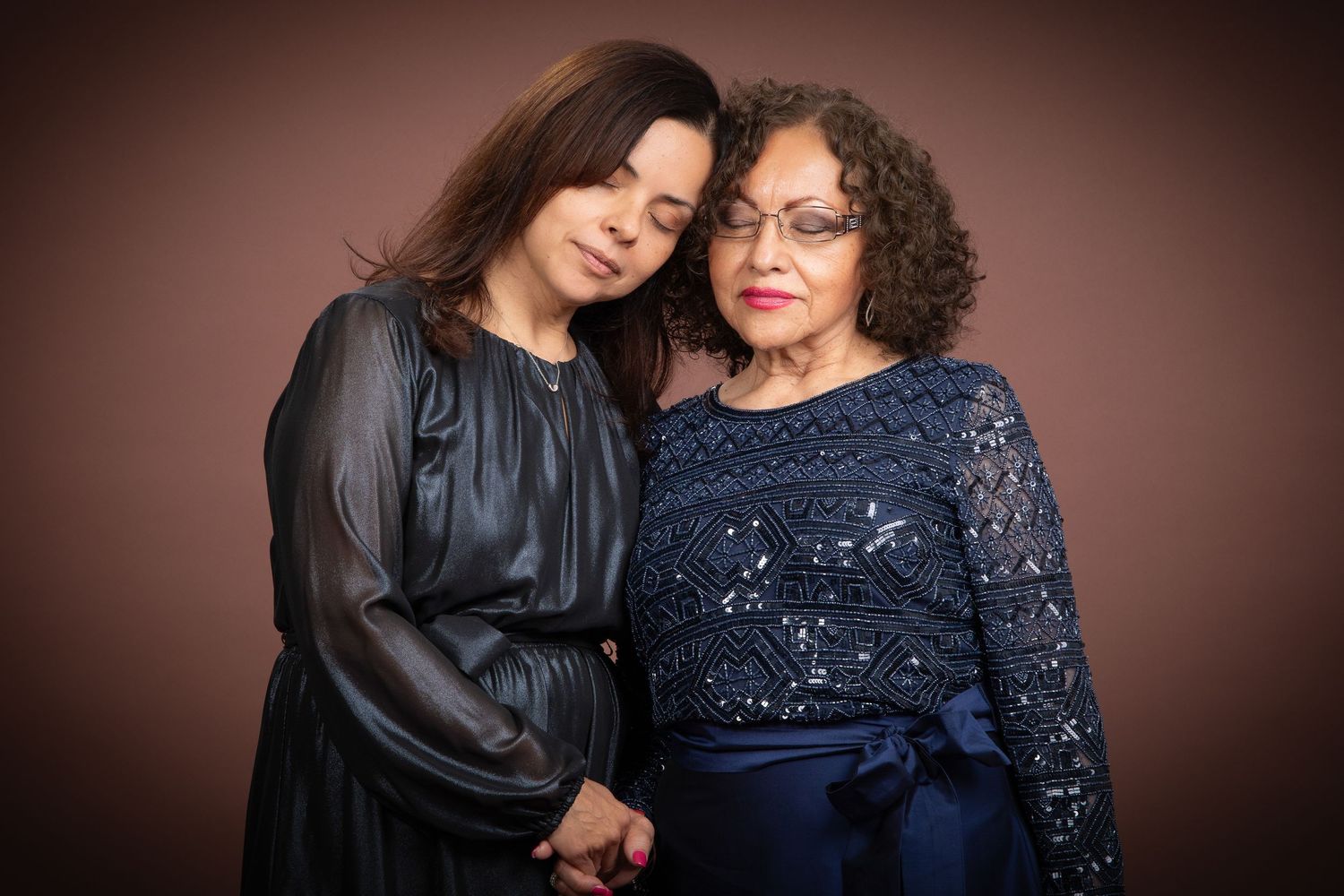 Young woman resting her head on an older womans shoulder holding hands in a studio portrait in the Bonsall Studio