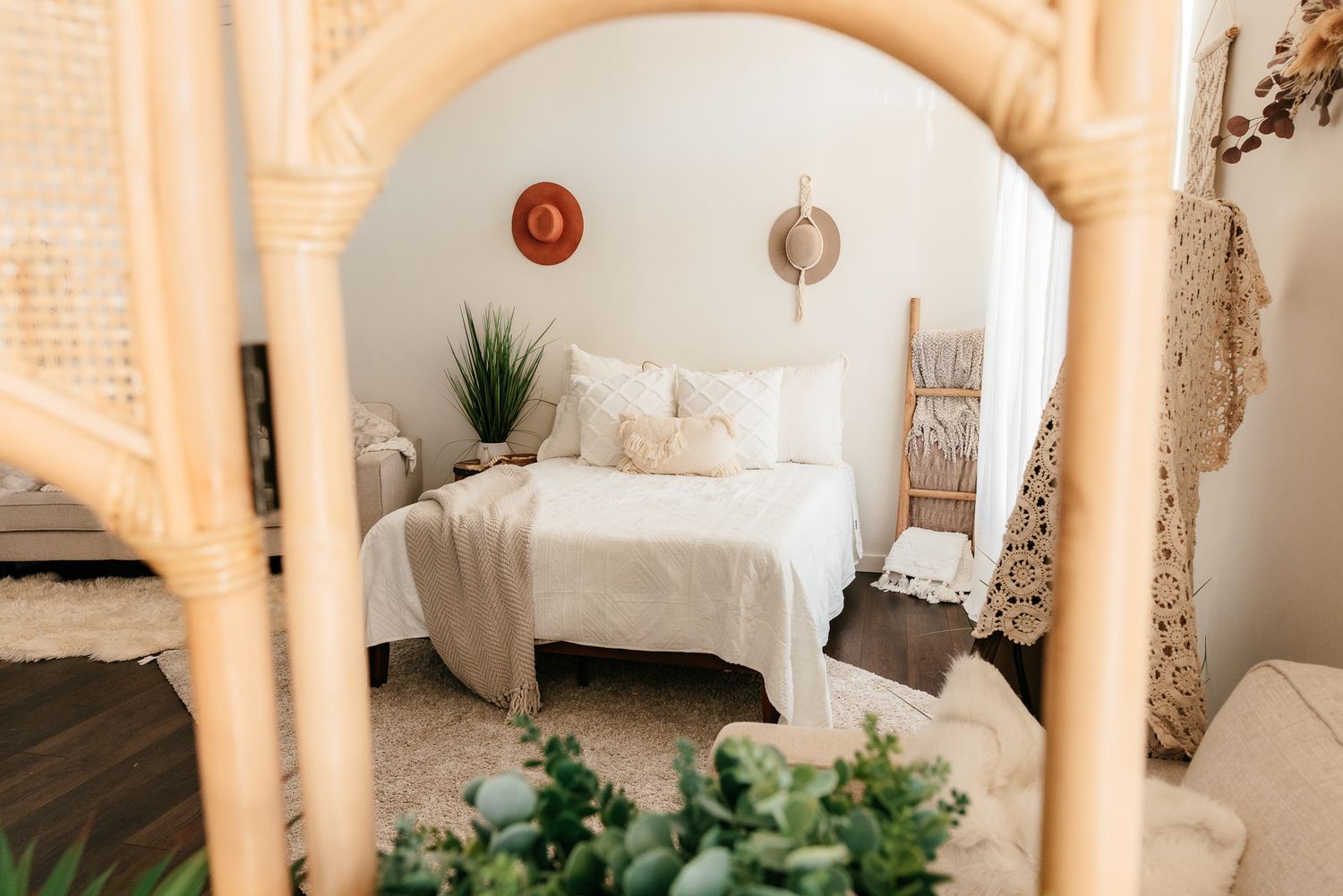 Boho photography studio reflected in rattan mirror showing white bed and neutral decor elements in the Bonsall Studio near Temecula