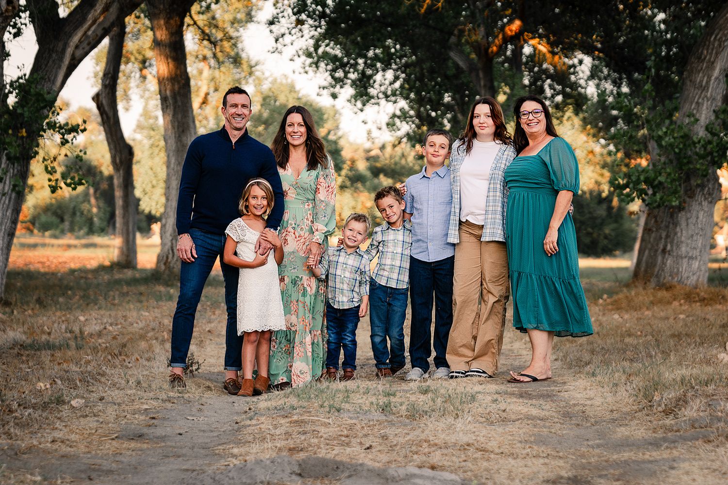 Extended family of eight smiling together on a sunny tree-lined dirt path in summer at the Bonsall Preserve.