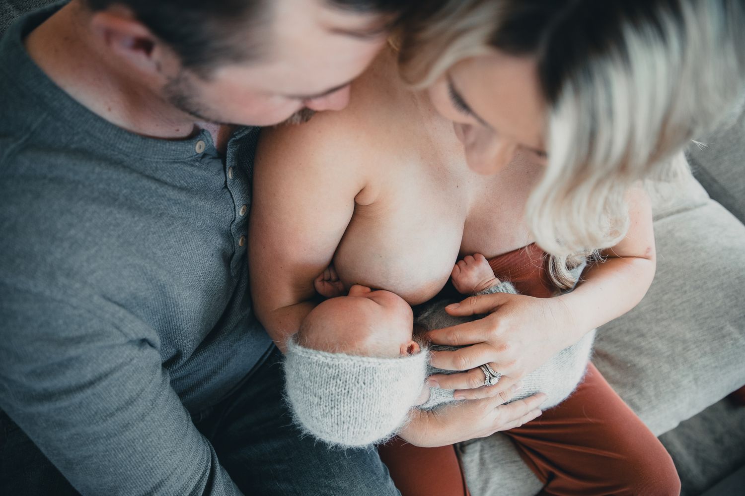 Parents lovingly kiss their newborn baby together, captured in a tender overhead lifestyle newborn photography session.