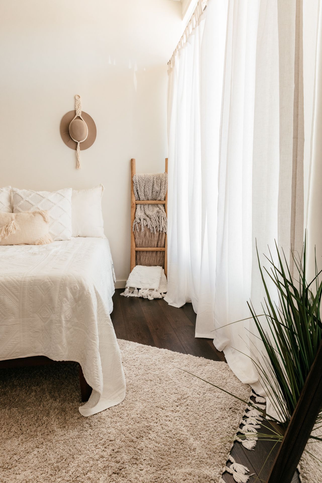 Minimalist boho bedroom corner with white bed, decorative ladder, sheer curtains, and a straw hat. in the Bonsall Studio near Fallbrook, Vis