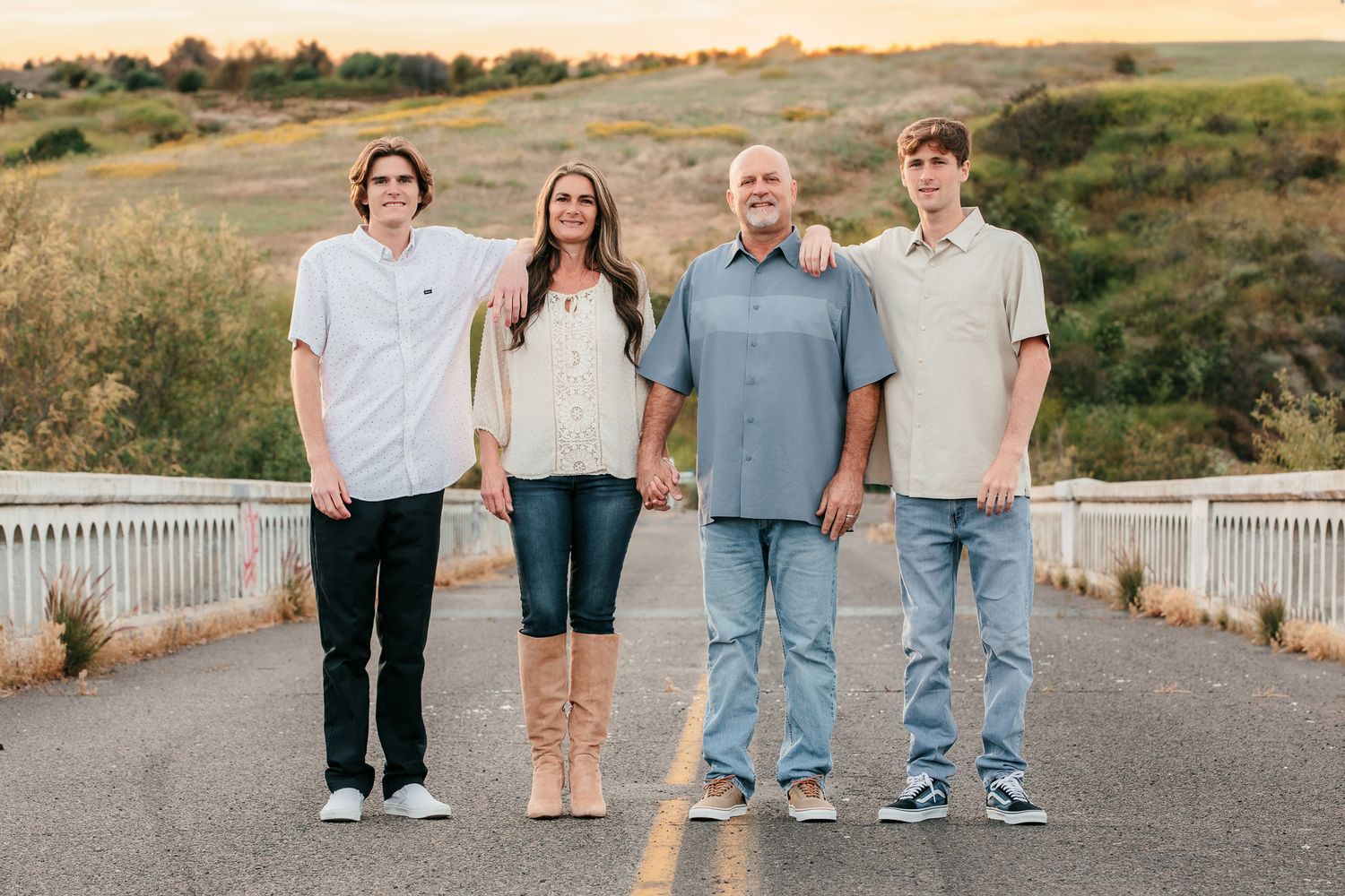 Family of four holding hands standing on rural road with rolling hills background.  In Bonsall, near Oceanside