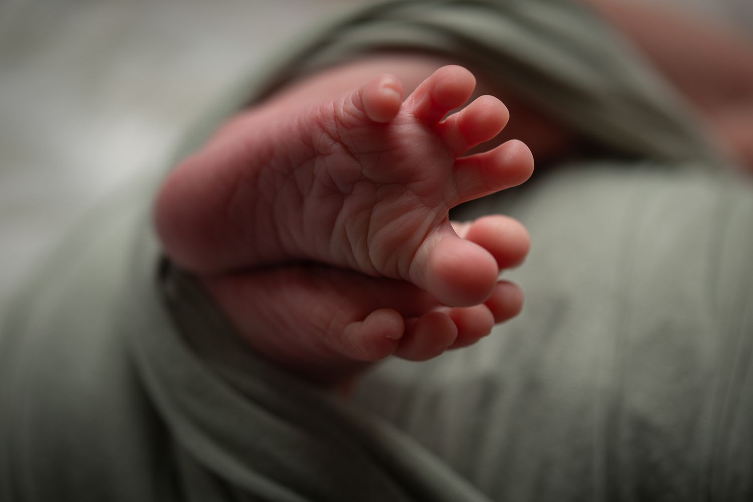 Close-up of tiny newborn baby feet wrapped in a soft green swaddle blanket. Fallbrook CA newborn photography studio offering posed baby