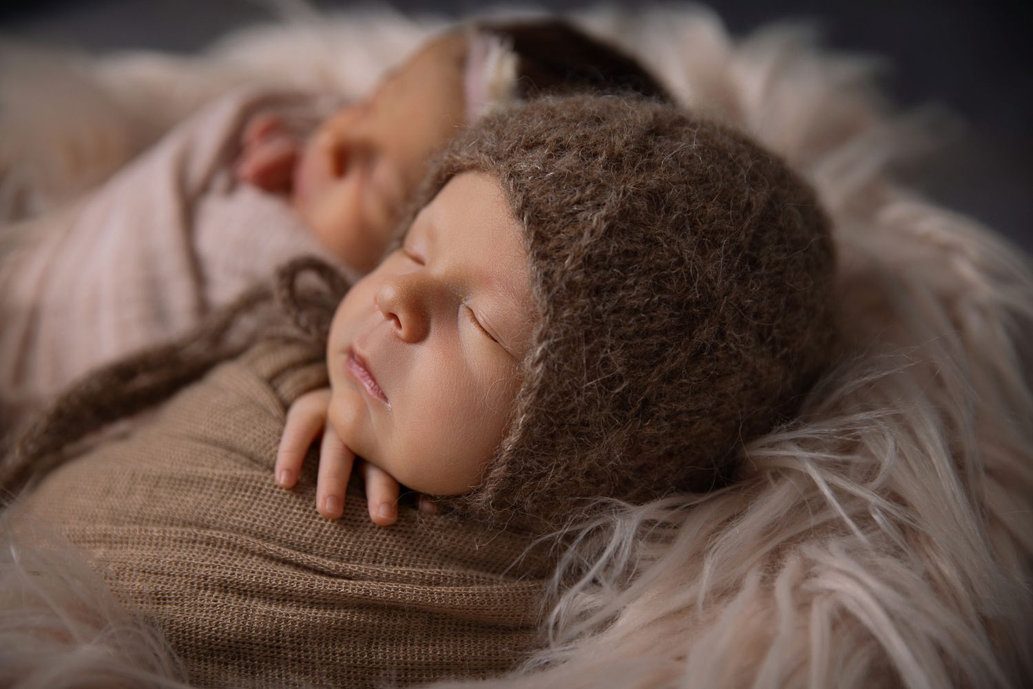 Sleeping newborn baby wearing brown fuzzy bonnet wrapped in tan swaddle on fur blanket at The Studio Bonsall, near Camp Pendleton Oceanside