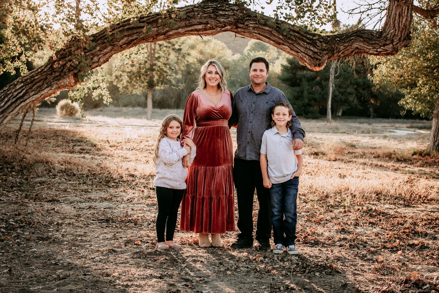Family of four posing under curved tree branch in autumn park setting at the Bonsall Preserve.