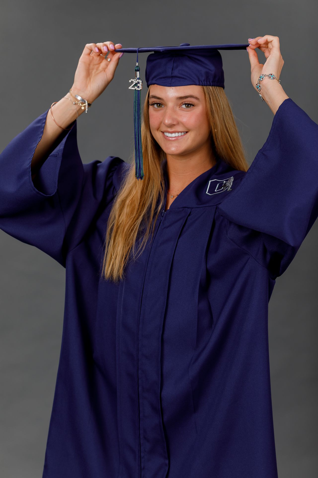 Smiling young woman in navy blue graduation cap and gown holding tassel for class of 2023 senior portrait.
