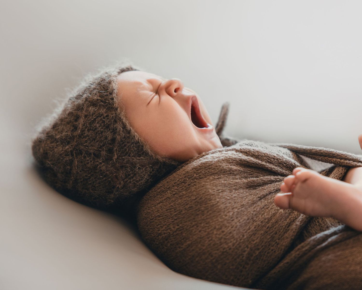 Newborn baby boy wrapped in brown yawning in the Bonsall Studio near Temecula