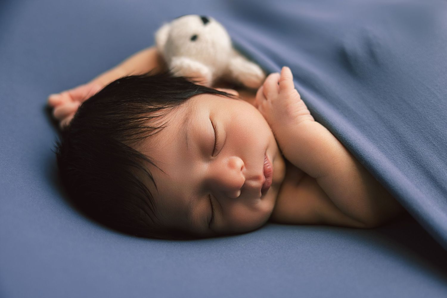 Newborn baby sleeping on a blue blanket with a small white stuffed bunny toy.