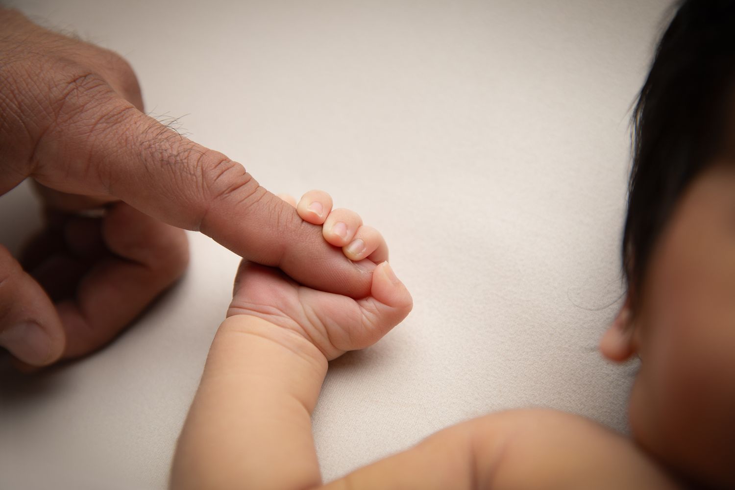A baby gently gripping an adult finger, showcasing the tiny delicate hand of a newborn in a tender bonding moment.