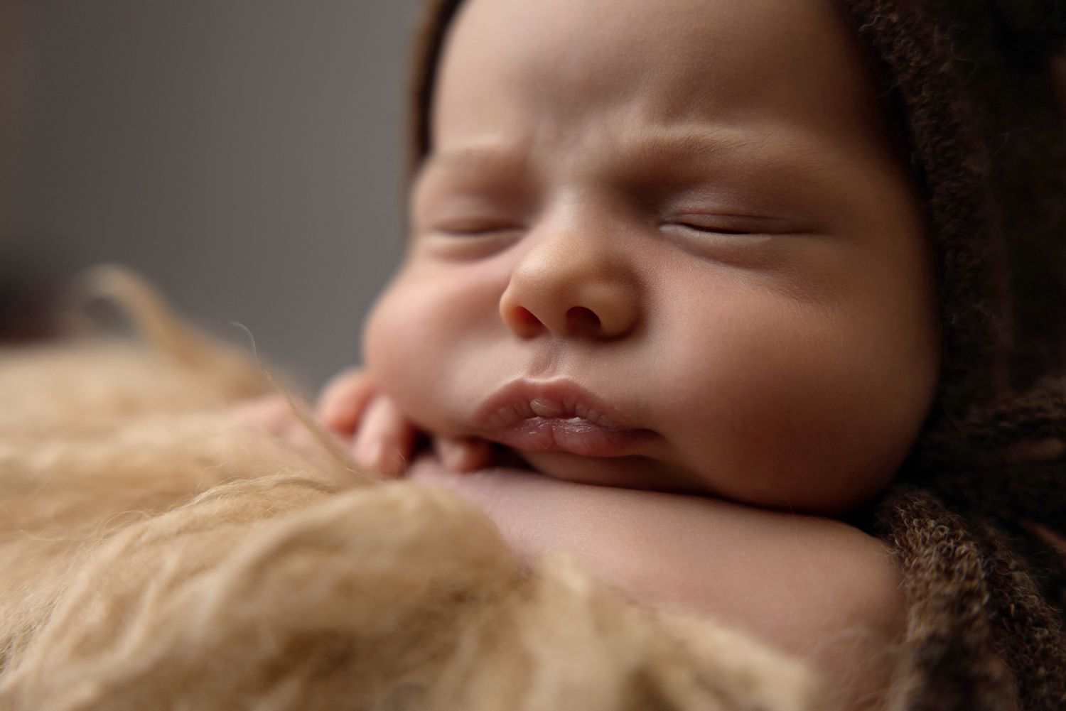 Peaceful newborn baby sleeping on soft fur blanket, wearing brown knit hat, close-up portrait photography.