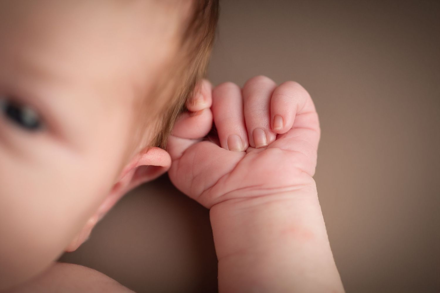 Close-up of a newborn baby's tiny hand and fingers resting gently against their cheek.