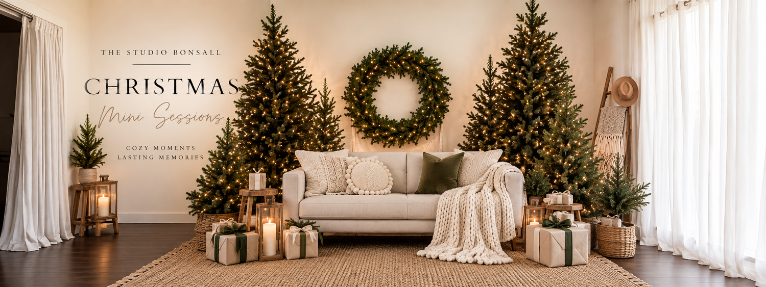 Elegant living room Christmas mini session backdrop with decorated trees, wreath, and gifts on a neutral sofa.