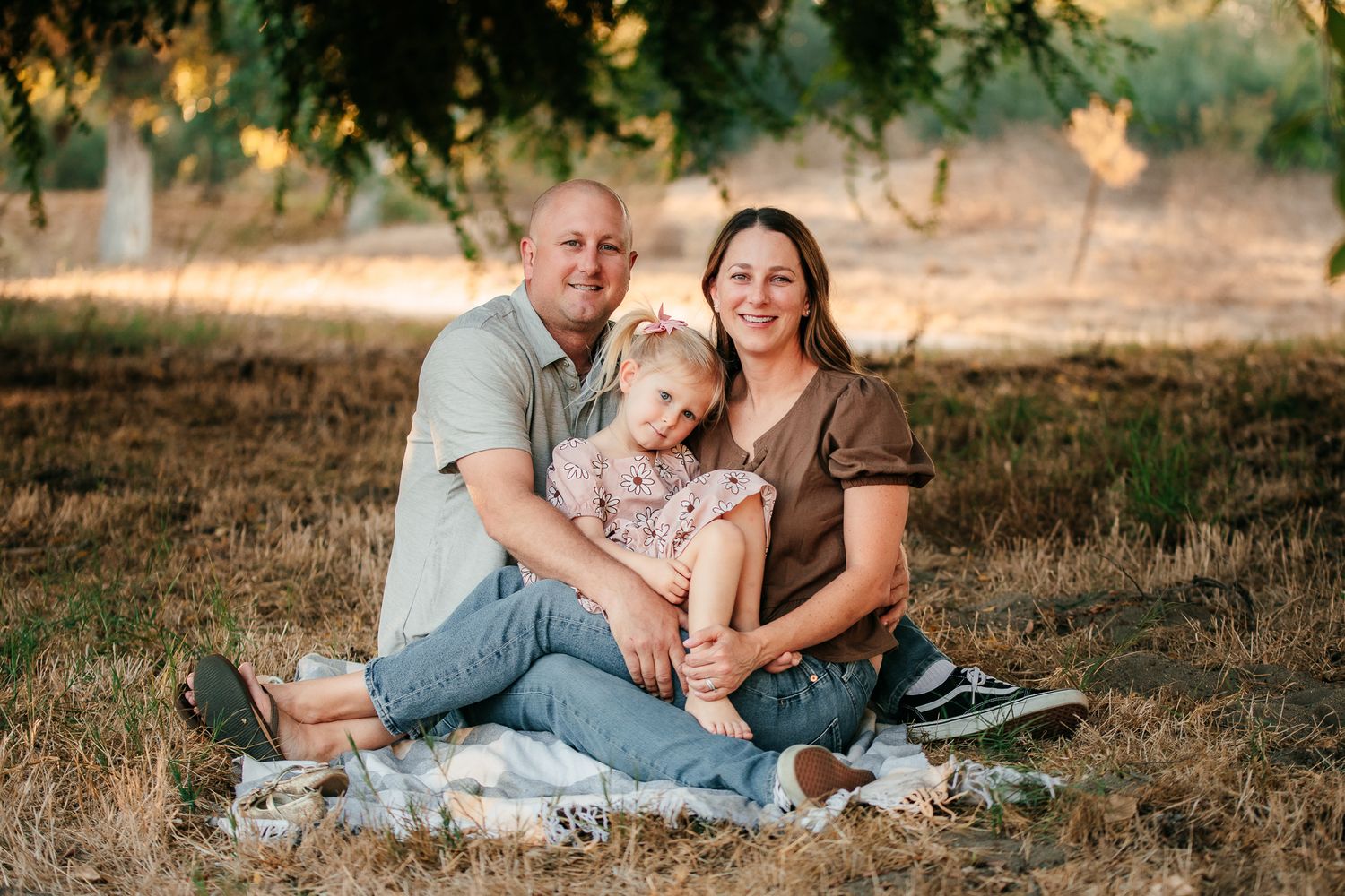 Couple sitting on blanket in orchard holding young daughter in warm sunset light.  In Bonsall, near Oceanside