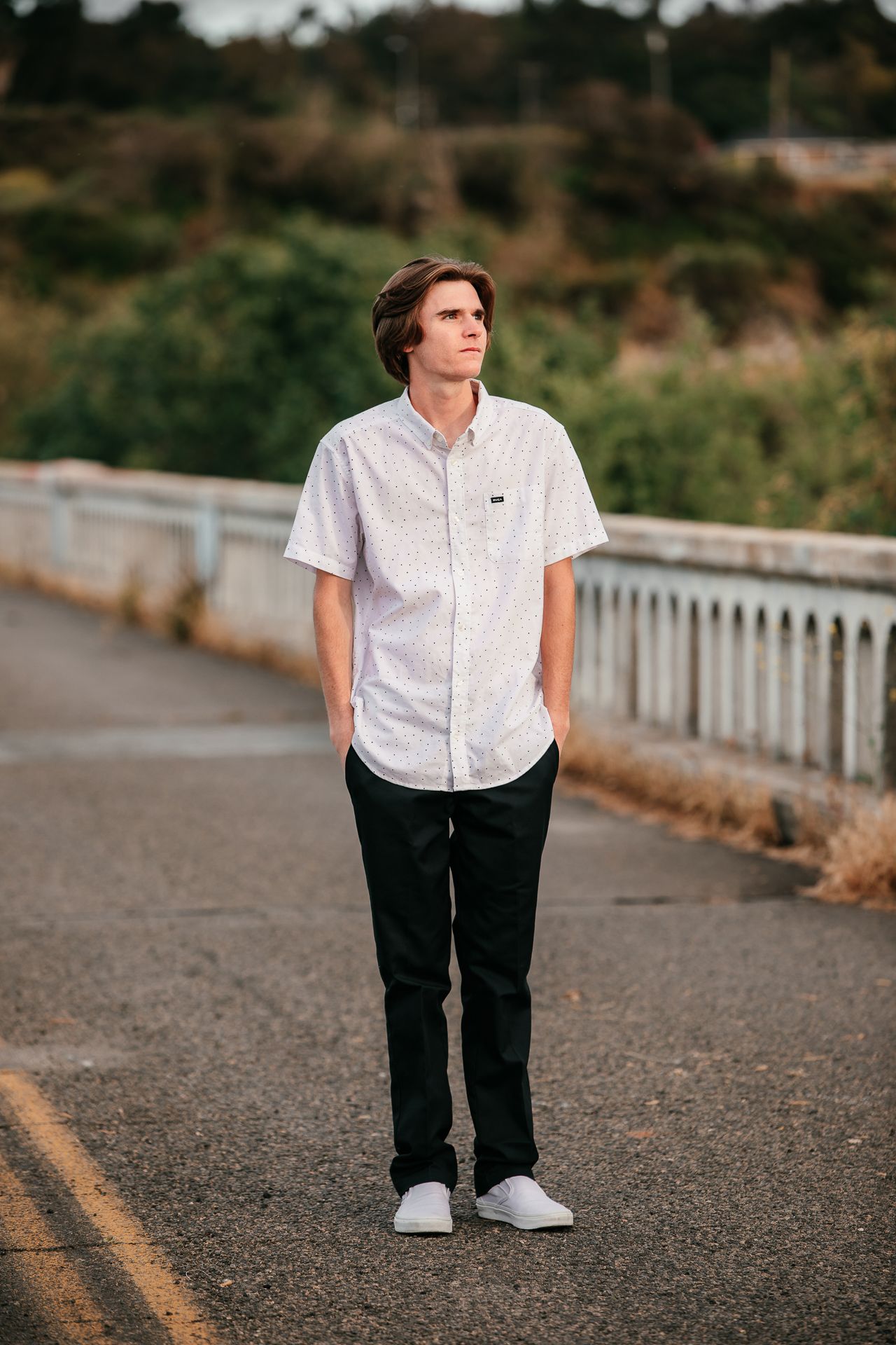 Young man in white button-up shirt and black pants standing on road for senior portrait photo session.
