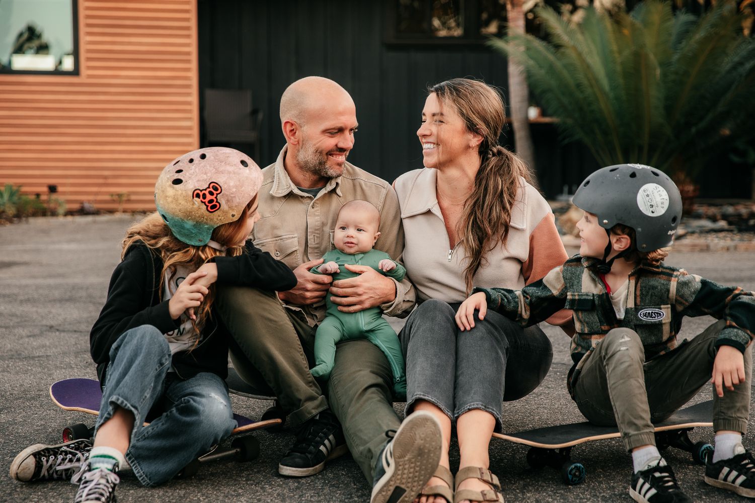 Fallbrook Photography takes family photos at home on skateboards, sharing tender moments and laughter during a casual outdoor photoshoot.