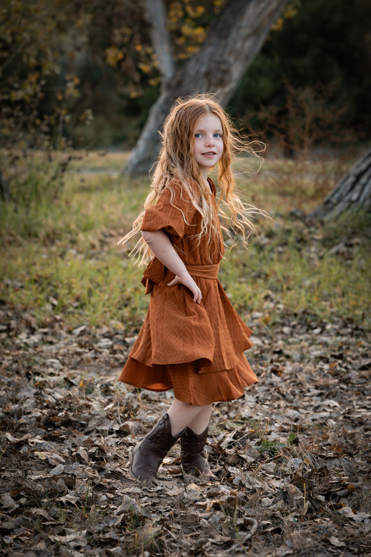 Young girl in rust dress and boots twirling in autumn leaves outdoors at the Bonsall Preserve.