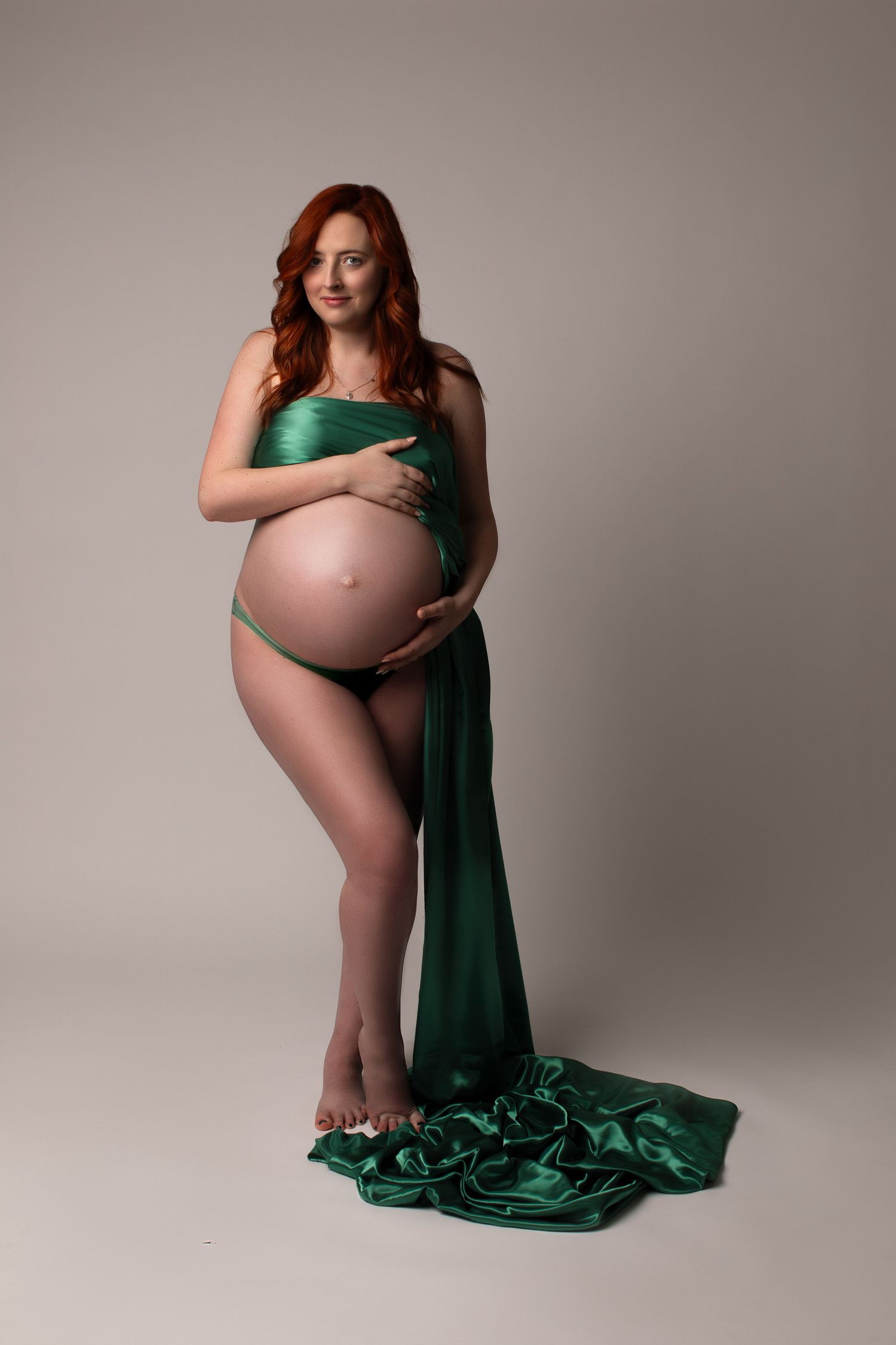 Pregnant redhead woman wrapped in green satin fabric on grey background. Bonsall, near Fallbrook, & Temecula