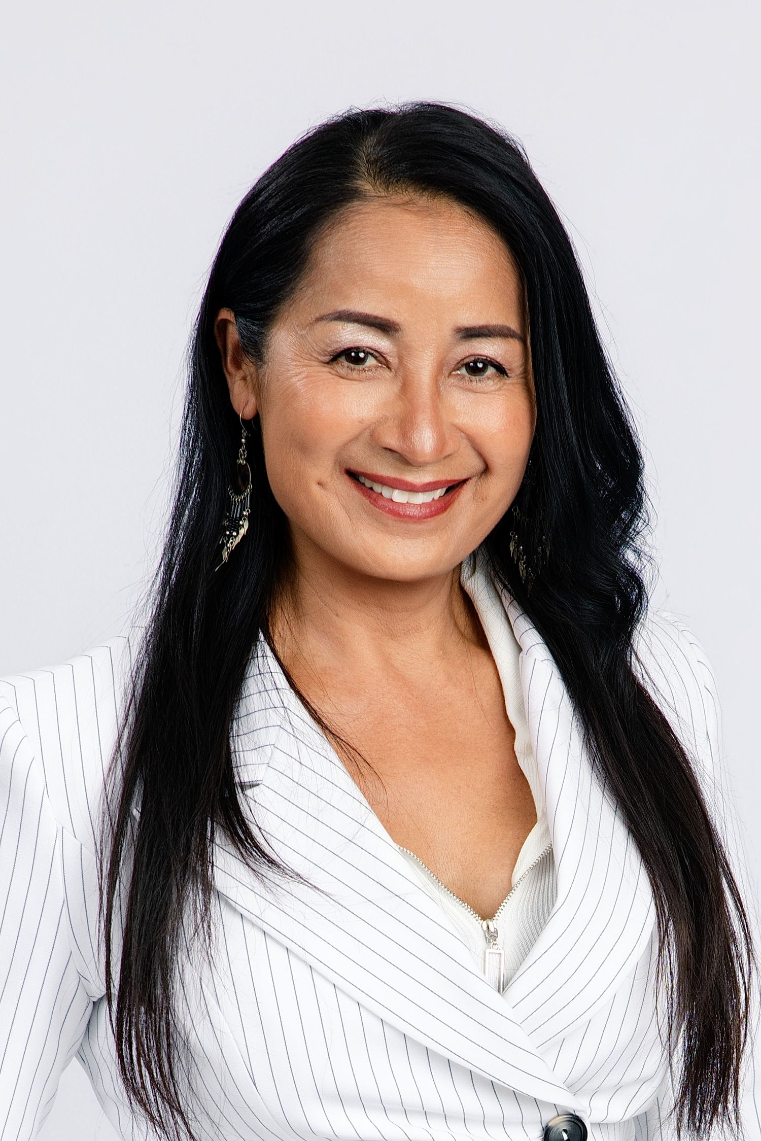 Professional headshot of a smiling woman with long black hair wearing a white pinstripe blazer against a gray background.
