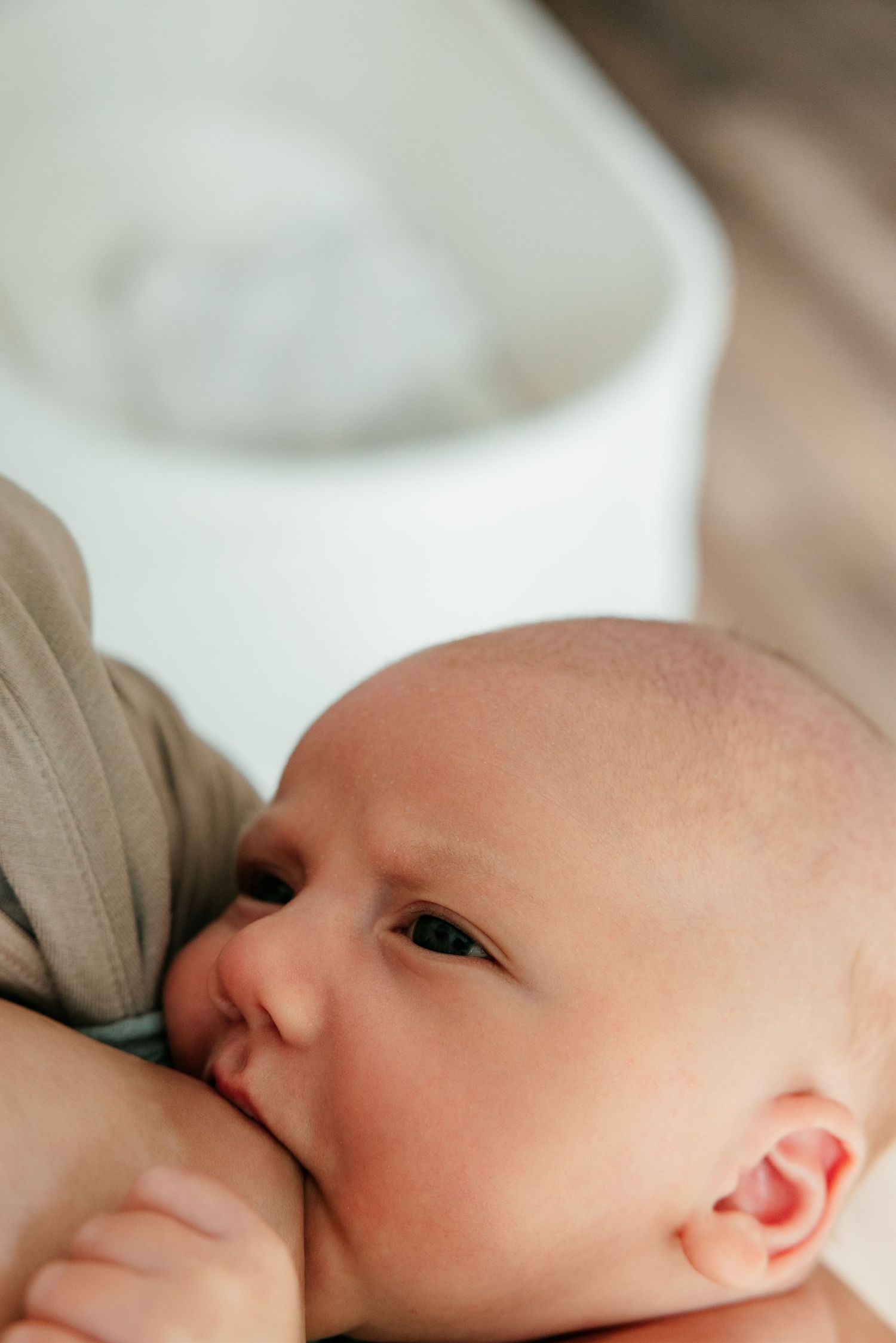 Close-up of a newborn baby breastfeeding, with soft focus background showing a white bassinet.
