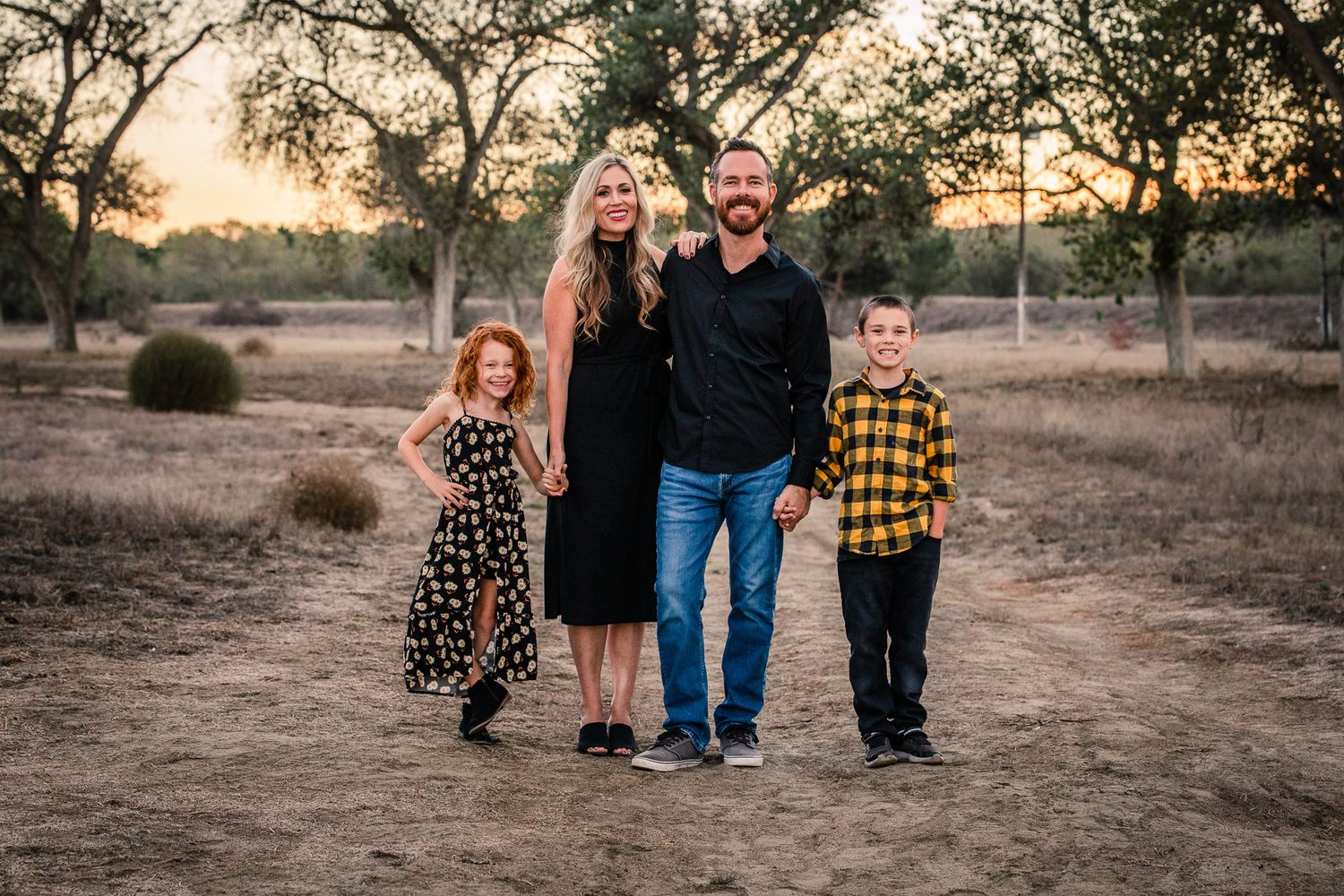 A family of four poses at sunset in a dry field, with two children and parents dressed in black at the Bonsall Preserve.