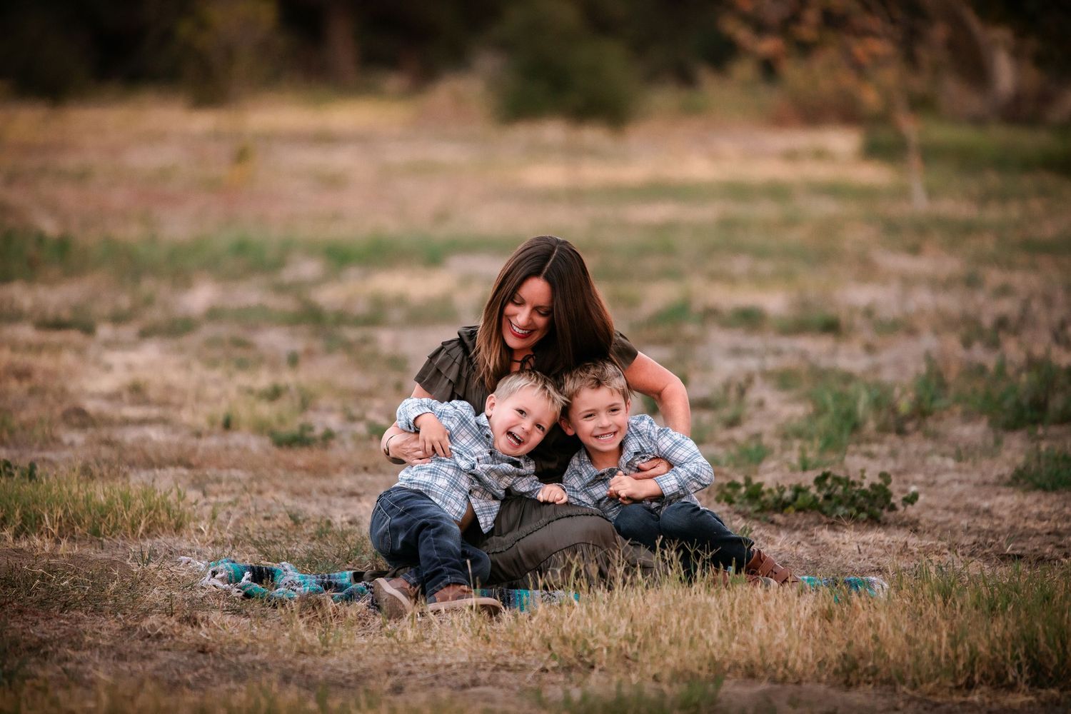 Mother sitting in a field hugging her two young sons during an outdoor family photo session.