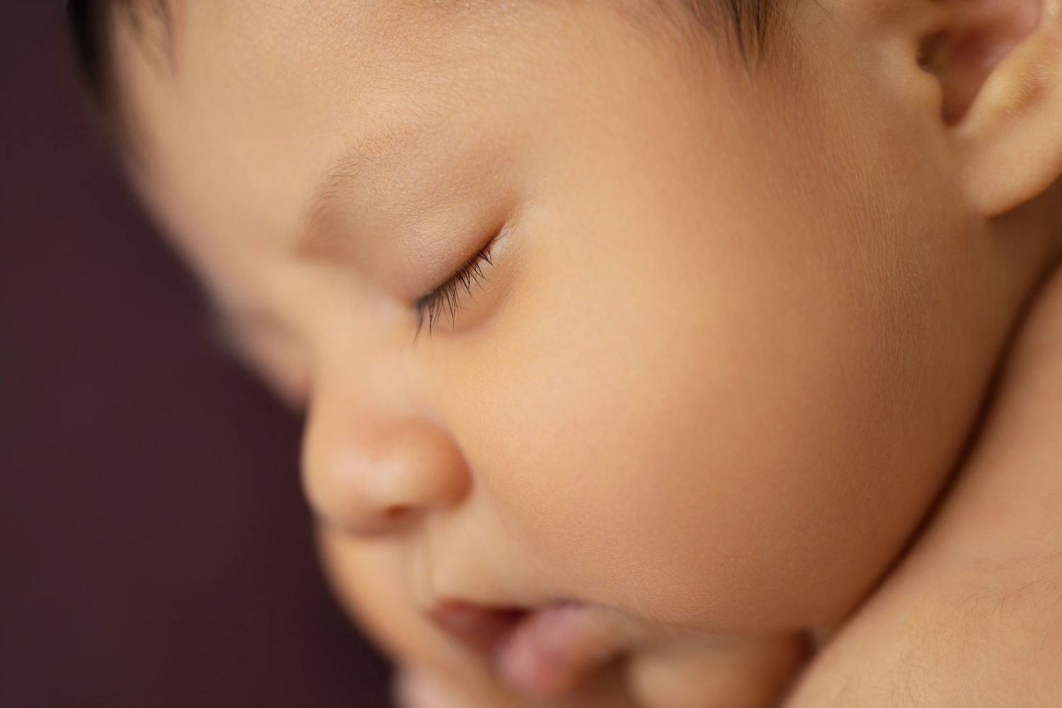 Close-up of a sleeping newborn baby with delicate features against a dark background.