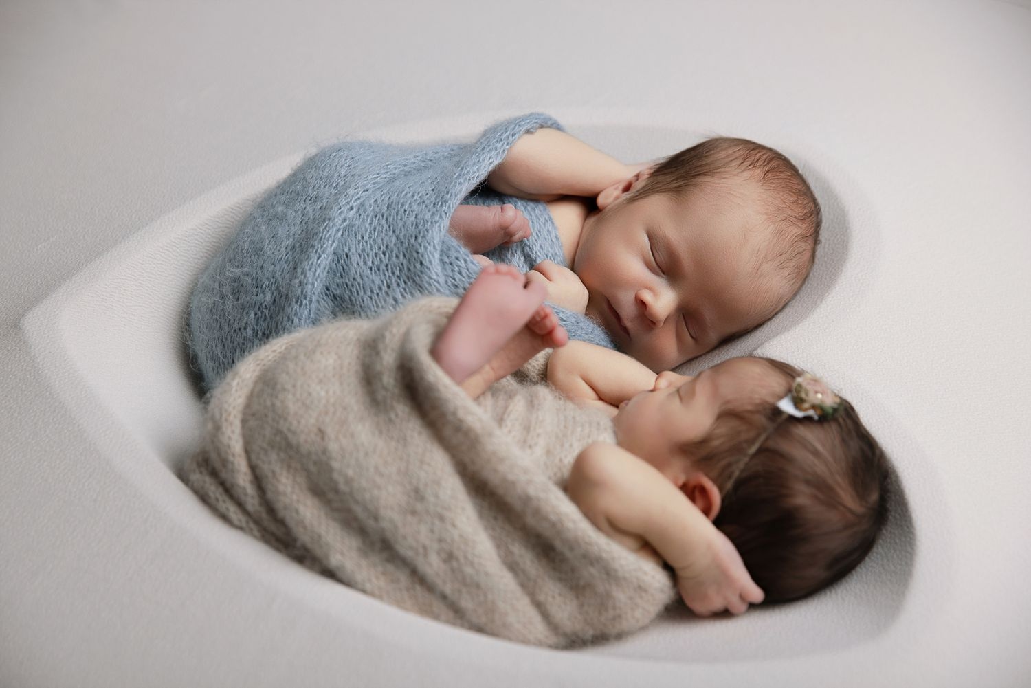 Twin newborns sleeping together in heart-shaped white bowl, swaddled in blue and beige wraps at The Studio Bonsall, near Camp Pendleton Ocea