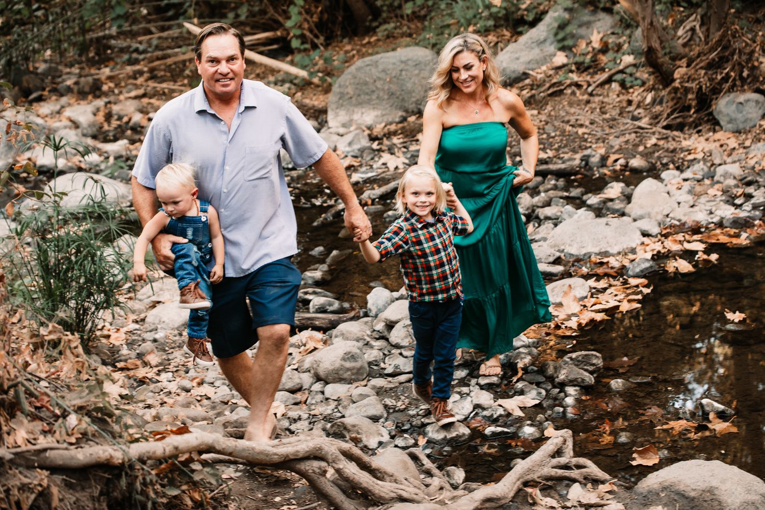 A barefoot family of four walks along a rocky creek bed in warm sunshine.