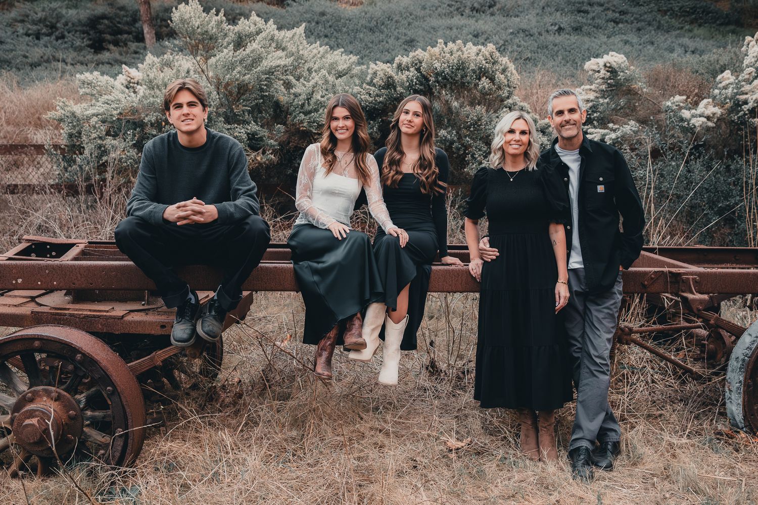 Family of five posing on a rustic wagon in a dry field.