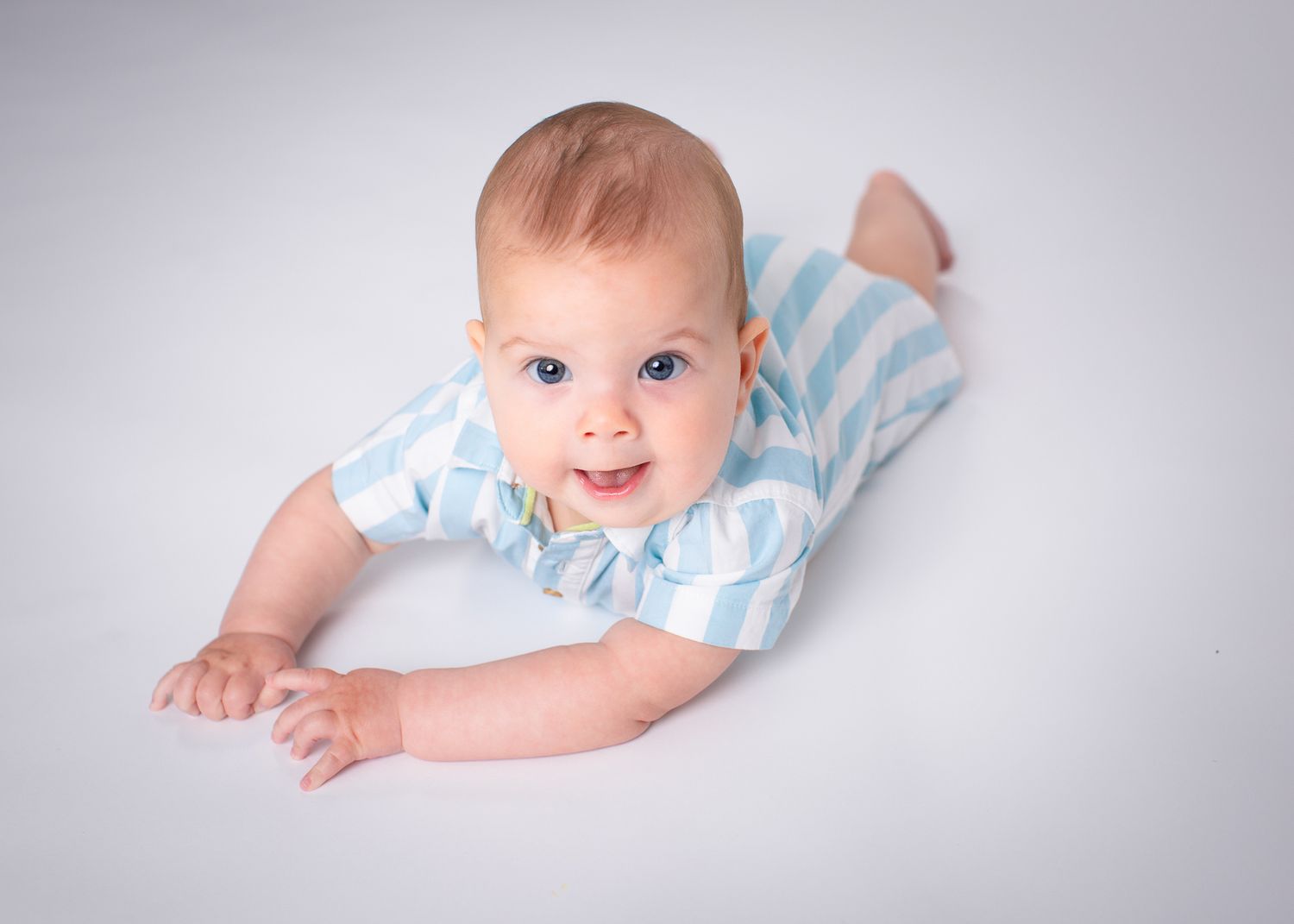 Adorable baby in blue striped outfit doing tummy time and looking up at camera.