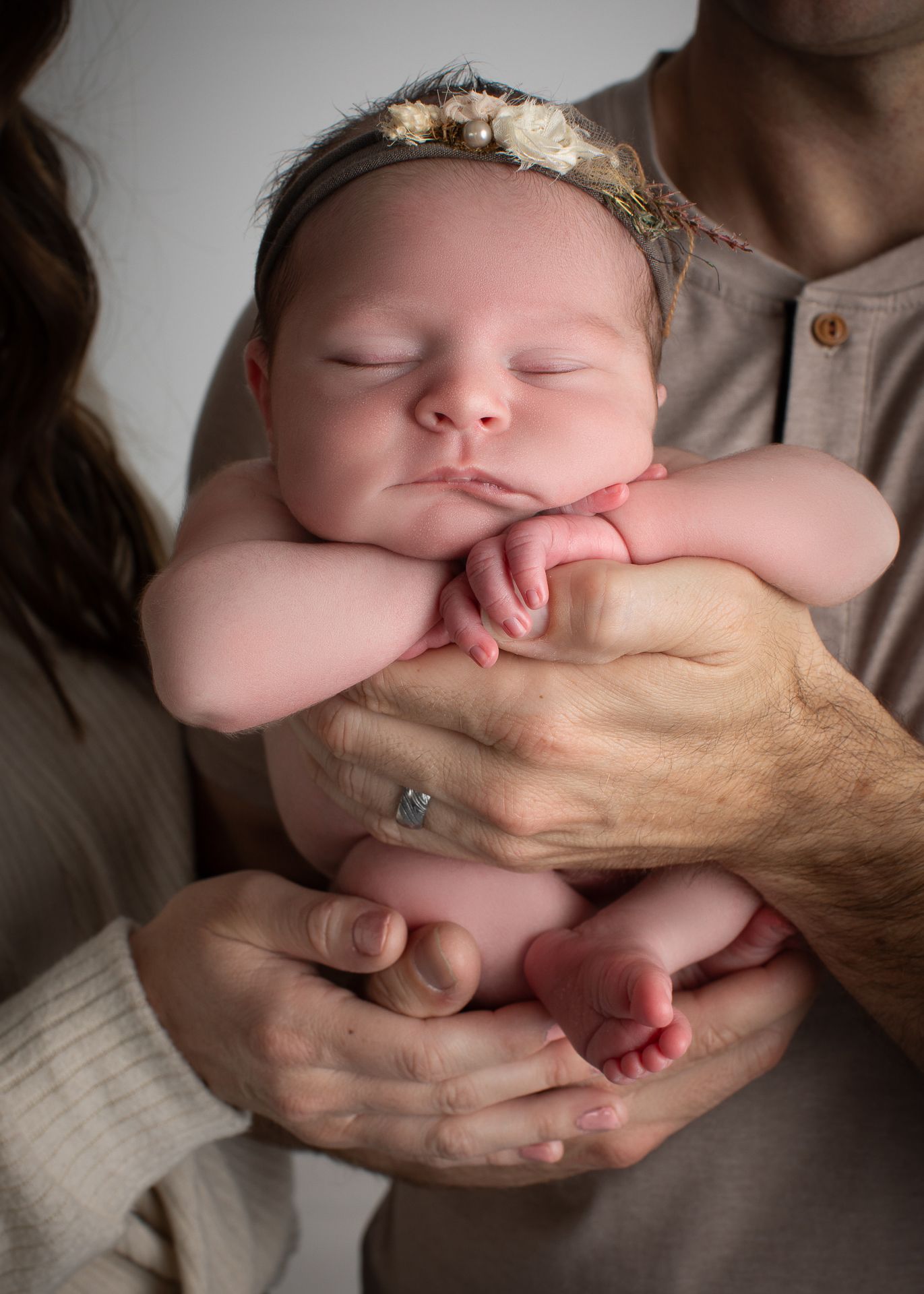 Sleeping newborn baby girl with floral headband cradled in parents hands during professional newborn photography session.