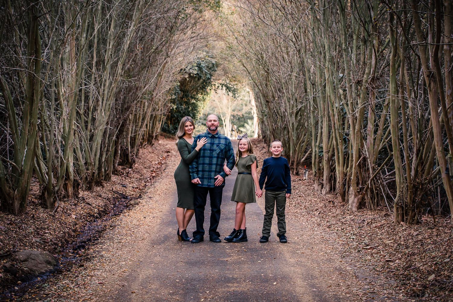 Family of four posing on leaf-covered path through arched bamboo tunnel, in Rainbow, CA