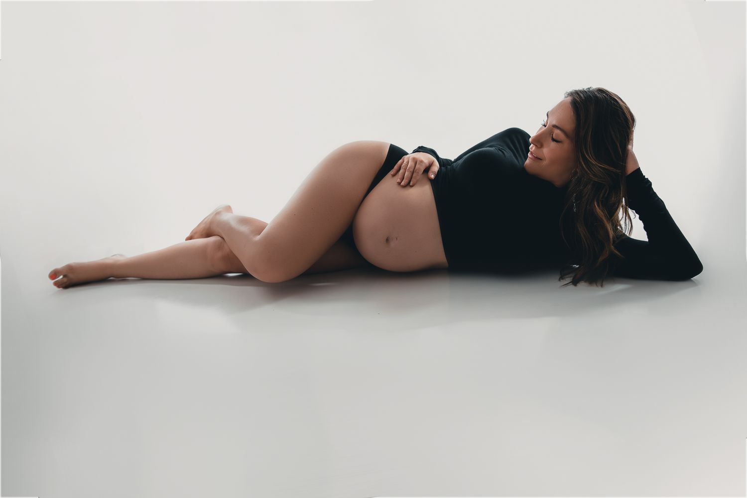 A black and white photo series showing a pregnant woman lying on the floor in different graceful poses.