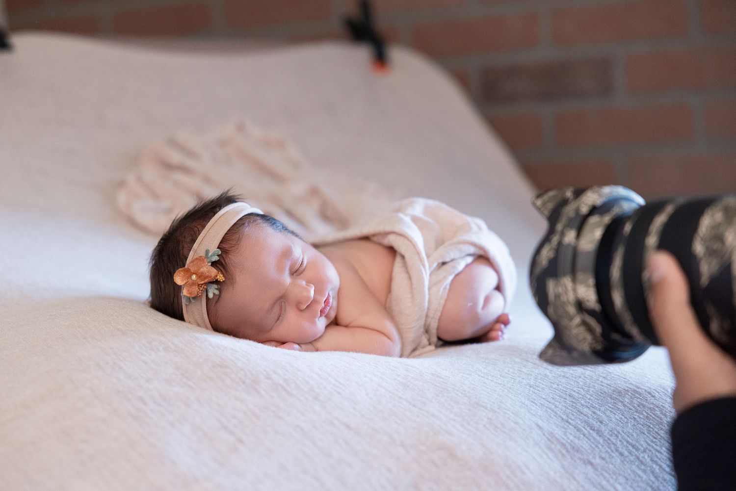 Newborn baby sleeping peacefully wrapped in white cloth with floral headband during professional photography session.