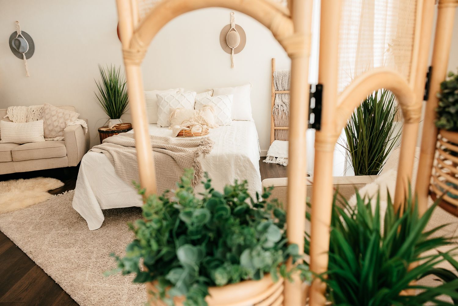 Boho bedroom viewed through rattan room divider with green plants and white bedding in background. in the Bonsall Studio near Fallbrook, Vis