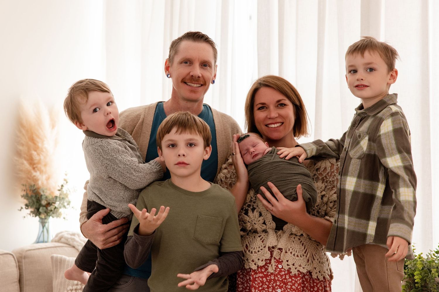Happy family of six posing indoors, parents holding four young children including a newborn baby, smiling together.