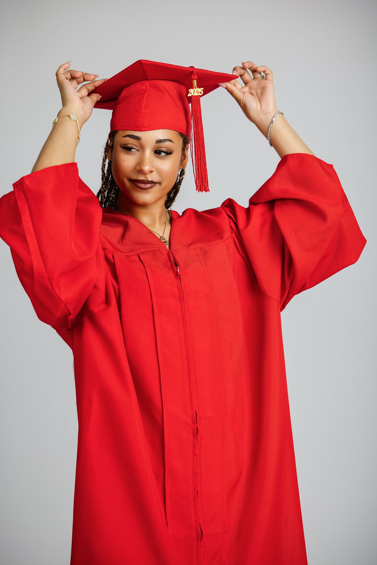 Graduate in red cap and gown adjusts her tassel while posing for a 2025 graduation portrait at the Studio Bonsall