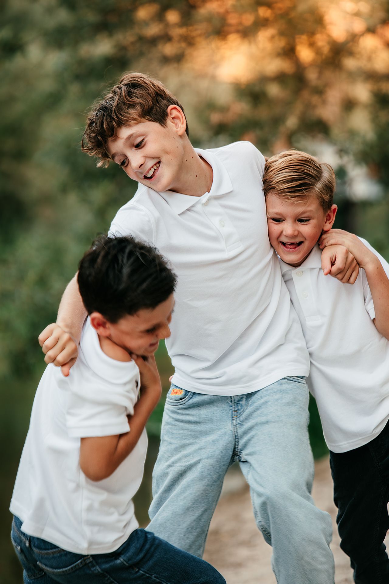 Three laughing boys in white polo shirts playfully wrestling together in a park at sunset in Fallbrook