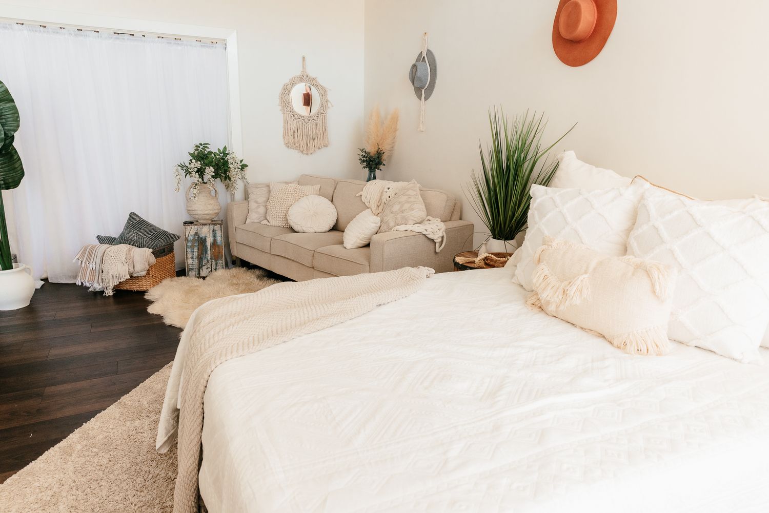 Close-up of boho bed with white textured pillows, cream bedding, and macrame wall decor in background. in the Bonsall Studio near Fallbrook,