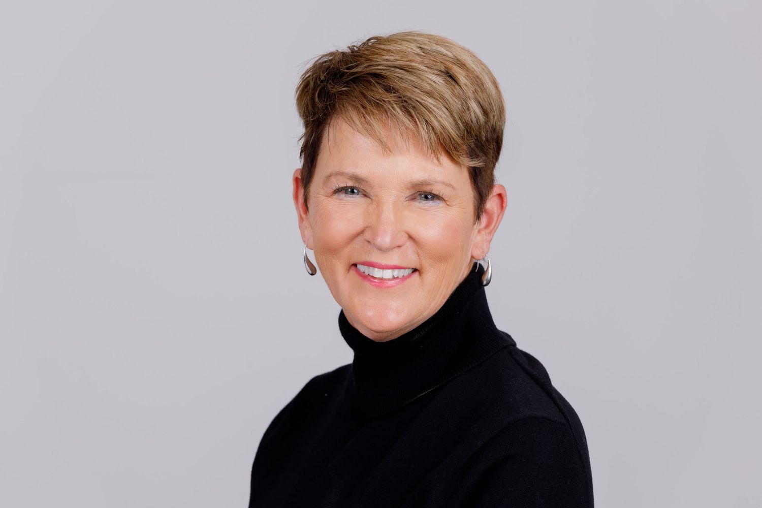 Professional headshot of smiling woman in black turtleneck on gray background in the Bonsall Studio near Fallbrook, Vista, Oceanside &