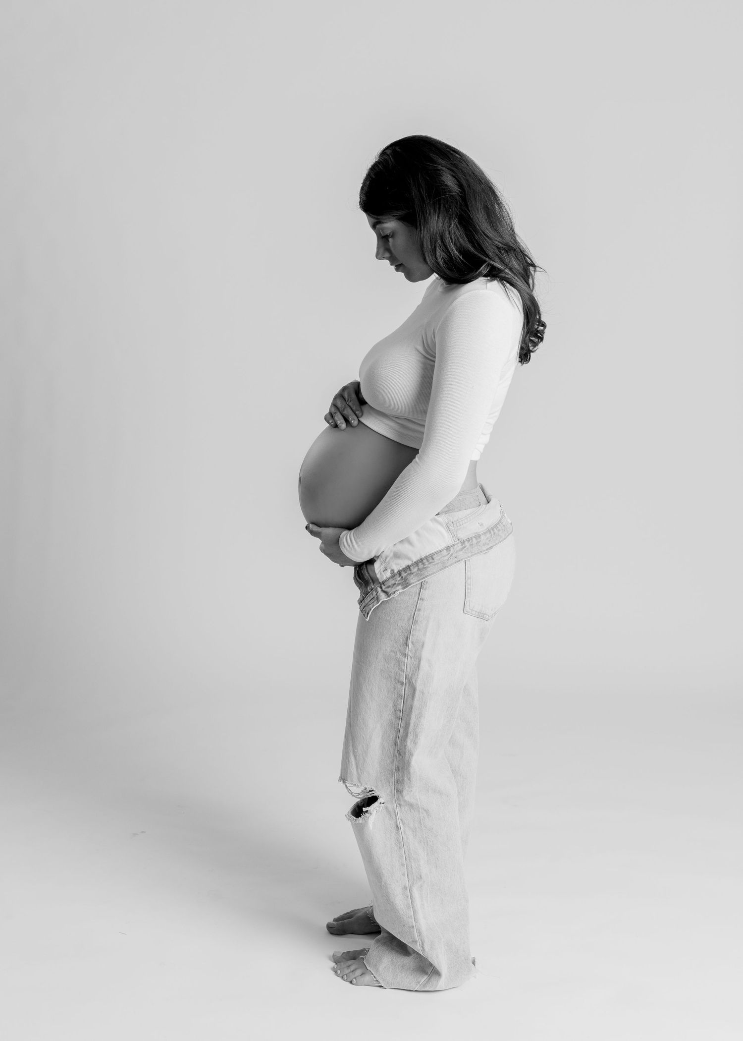 Black and white side profile of a pregnant woman in jeans cradling her baby bump in Bonsall, near Fallbrook, & Temecula