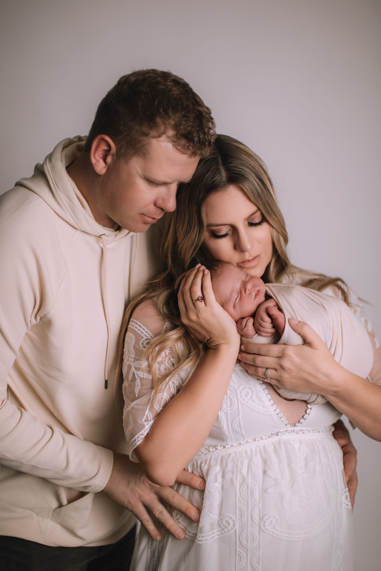 A couple in cream outfits tenderly gazes at their newborn baby during a studio portrait session.