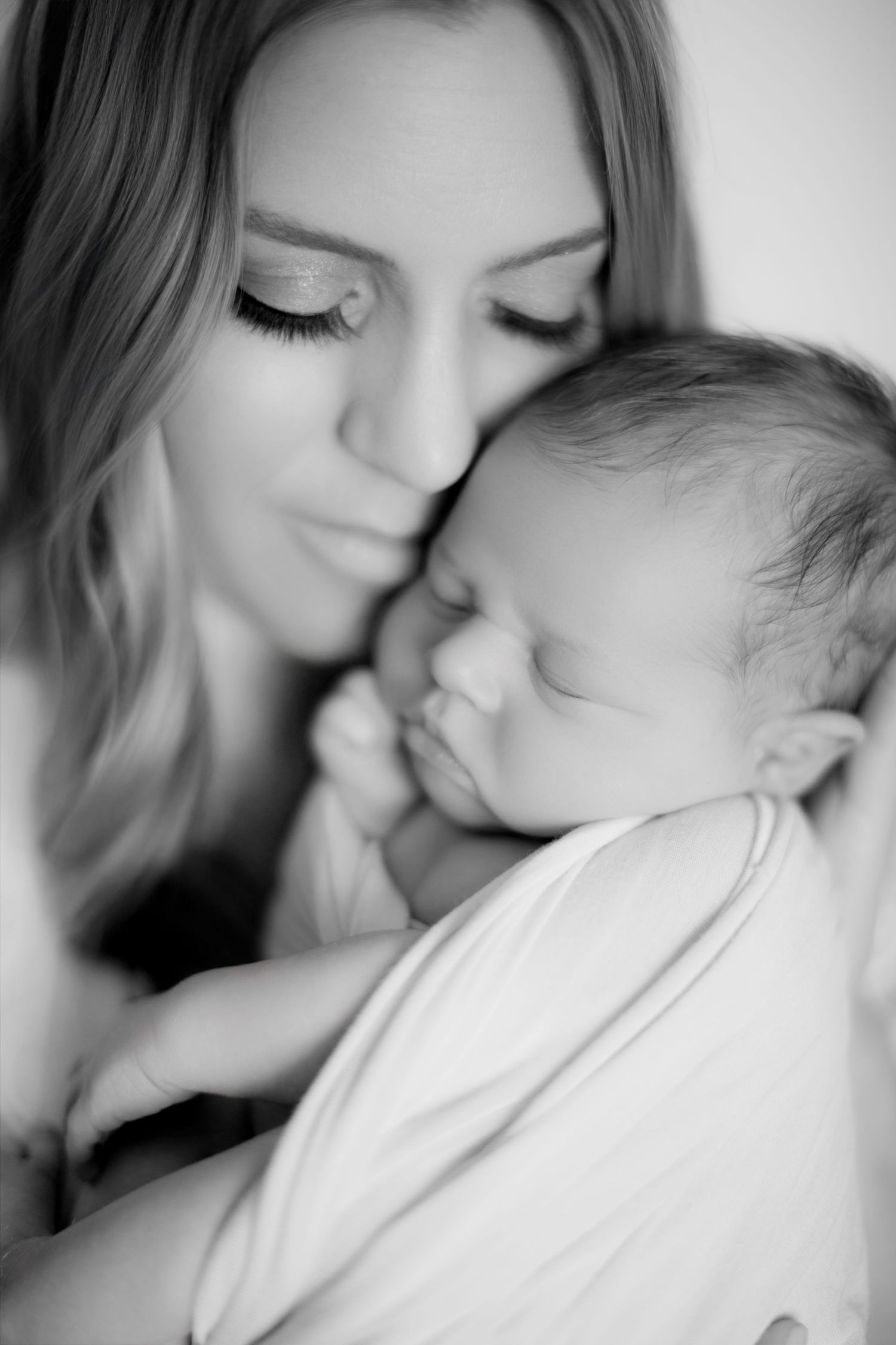 Black and white photo of a young mother tenderly holding her sleeping newborn baby close to her face.