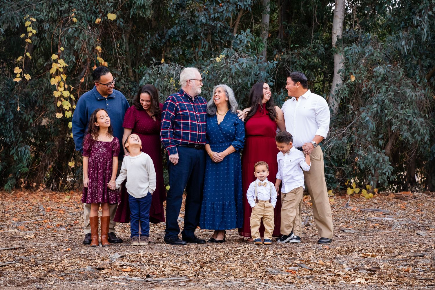 Extended multigenerational family portrait among fall foliage in park.