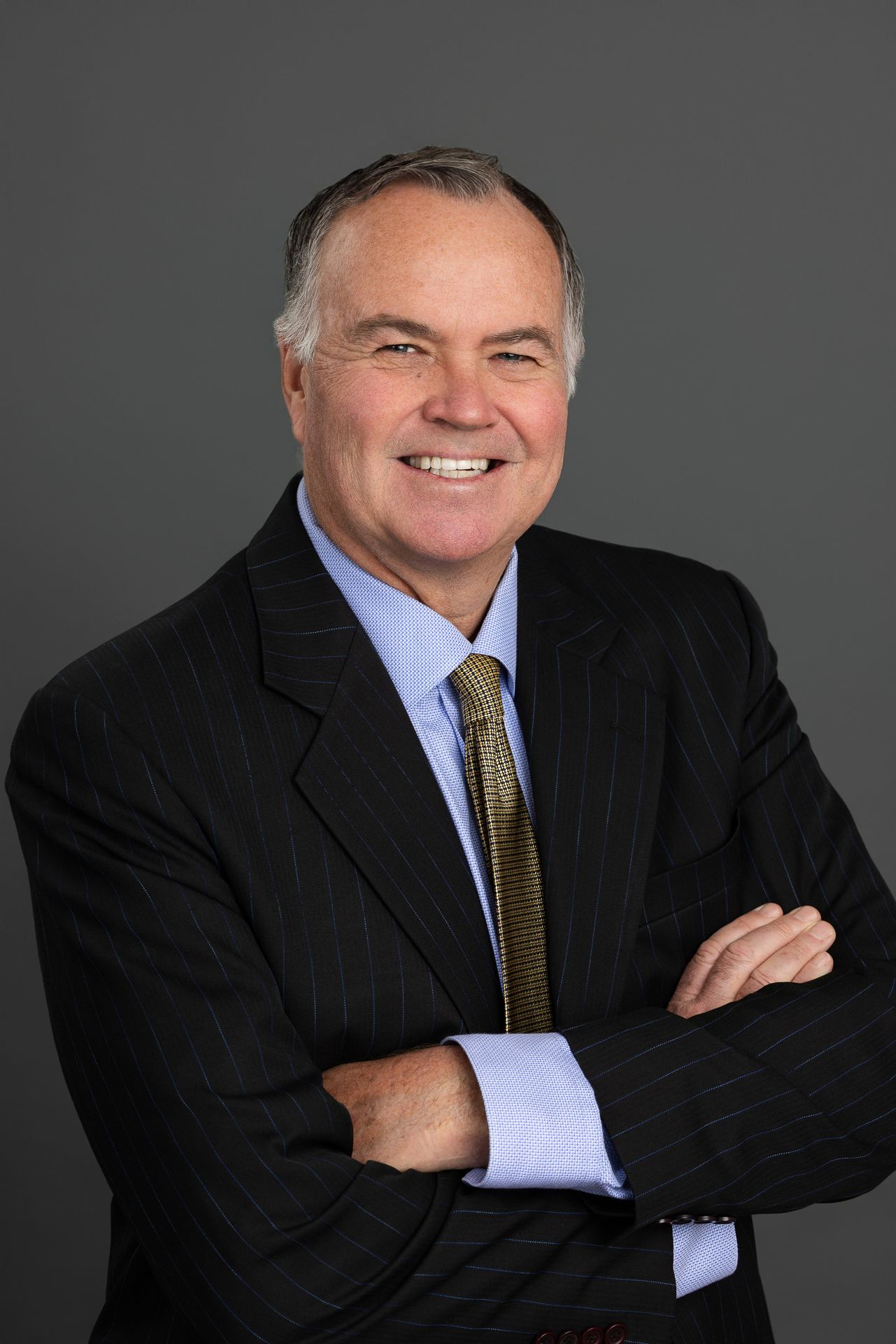 Professional headshot of smiling man in pinstripe suit, arms crossed in the Bonsall Studio near Fallbrook, Vista, Oceanside &
